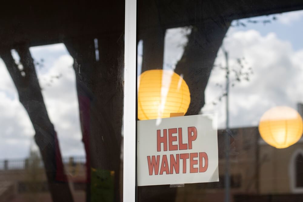 Now Hiring sign in a window on a street