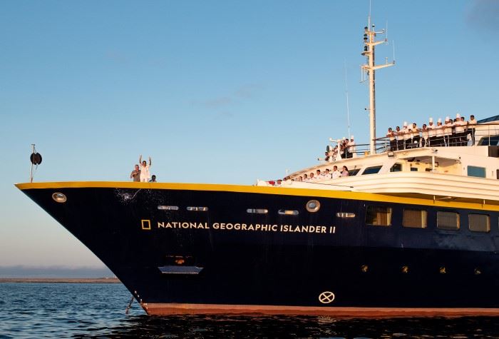 Angela Flaim smashes a bottle of champagne against the full of National Geographic Islander 2