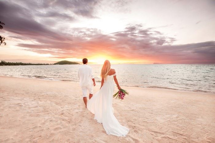 a newly married couple walking on a beach