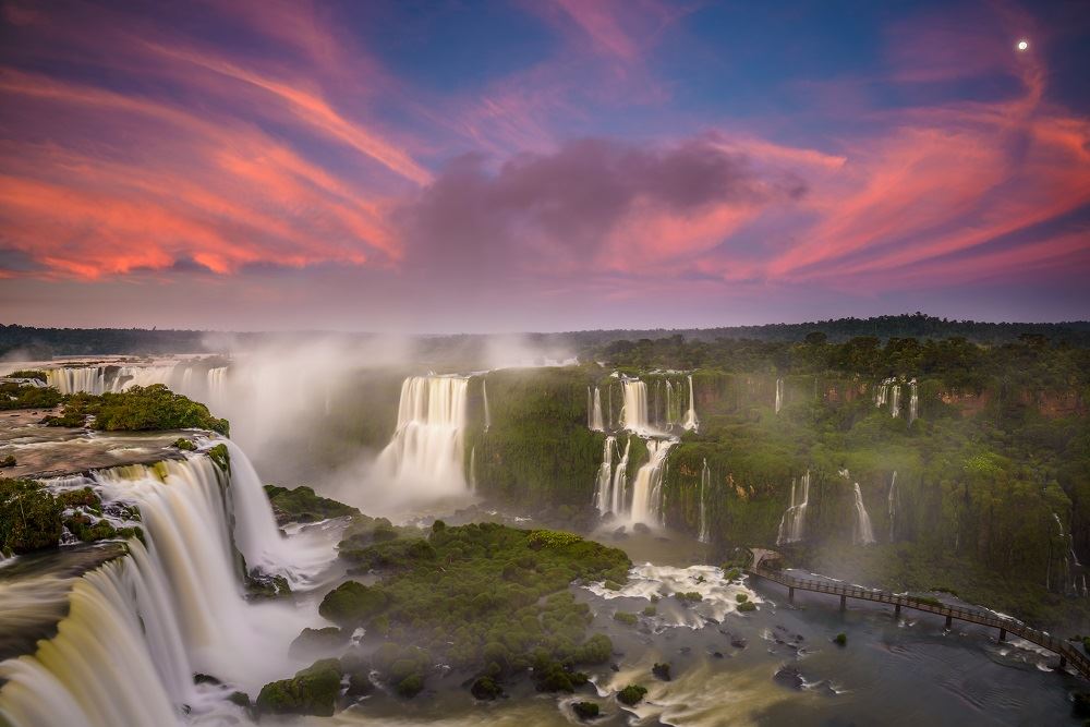 Iguazu Falls flowing with red sky behind it 