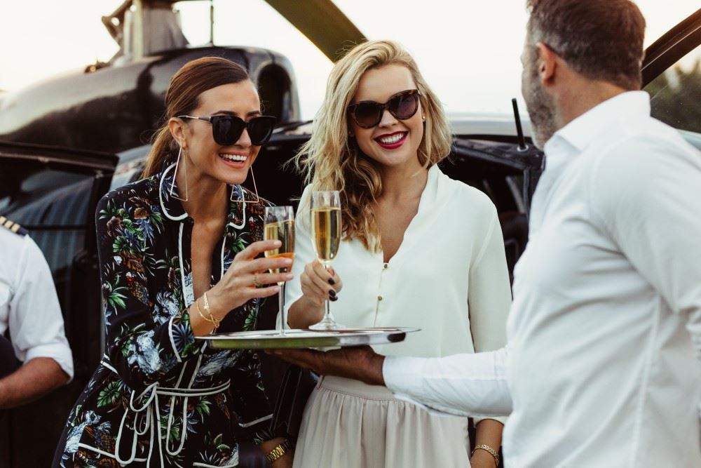 affluent mother and daughter greeted with champagne with helicopter in the background