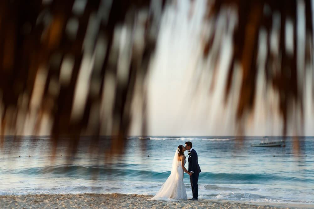 Destination wedding bride and groom kissing between palm trees 