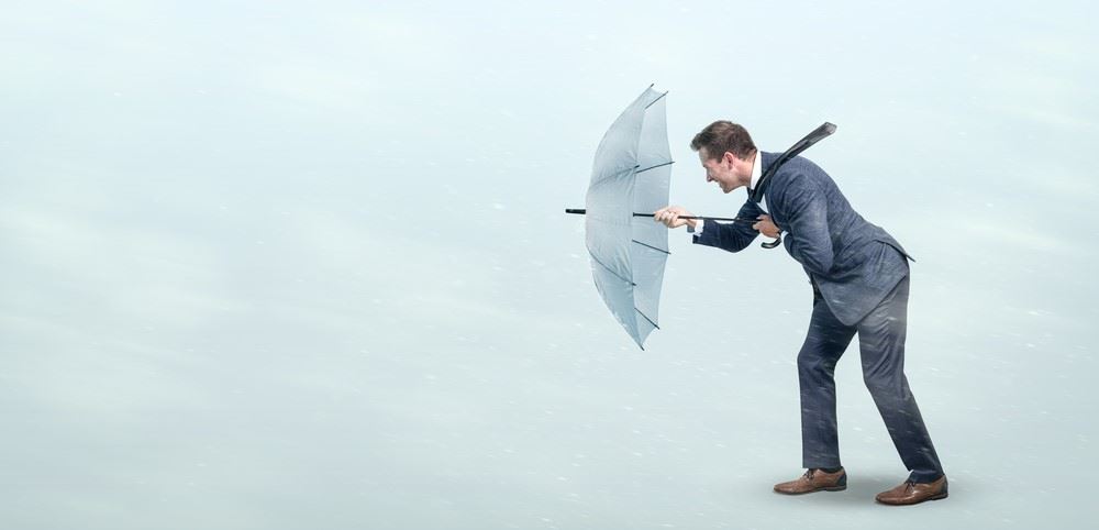a man holding an umbrella in front of him to fight against headwinds in business